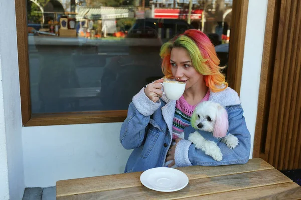 Young woman enjoying the morning cup of coffee with her maltese dog in a pet carrier backpack. Close up, copy space, background.