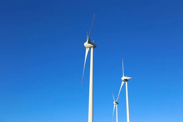 Cropped shot of three wind turbines over the clear blue sky background Green energy concept. Copy space for text, close up, low angle shot.