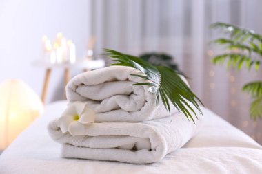 Masaj masasında bir yığın yumuşak havlu bekliyor. Spa salonu için sembolik nesnelerle kompozisyon. Kapat, kopyala boşluk, arkaplan.