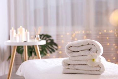 Masaj masasında bir yığın yumuşak havlu bekliyor. Spa salonu için sembolik nesnelerle kompozisyon. Kapat, kopyala boşluk, arkaplan.