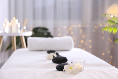 Sıraya dizilmiş siyah volkanik taşların yakın plan çekimi ve masaj masasının üzerine sarılmış bir havlu. Arka planda Bokeh ışıkları var. Boşluğu kopyala.