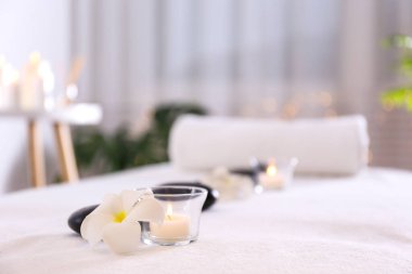 Sıraya dizilmiş siyah volkanik taşların yakın plan çekimi ve masaj masasının üzerine sarılmış bir havlu. Arka planda Bokeh ışıkları var. Boşluğu kopyala.