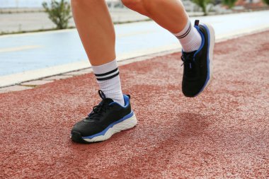 Tekstil zulmünden uzak ayakkabılar giyen ve koşu pistinin sentetik yüzeyinde koşu yapan kadın sporcunun kırpılmış görüntüsü. Kapat, kopyala boşluk, arkaplan.