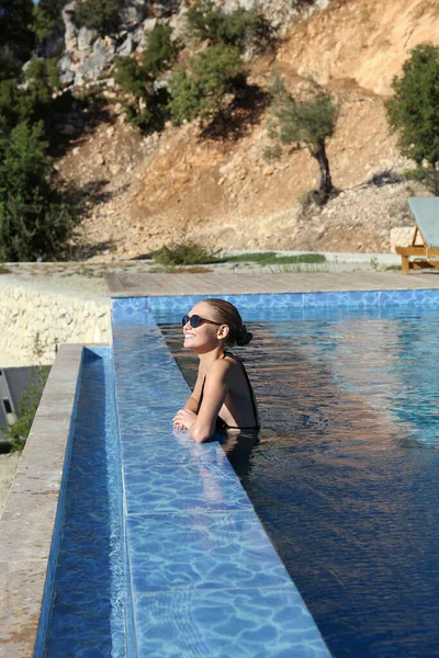 Manzaralı okyanusun ve özel villadaki sonsuz havuzun kenarından dağ manzarasının tadını çıkaran çekici genç bir kadın. Açık havuzda sıska bir kadın. Boşluğu kopyala, arkaplan.