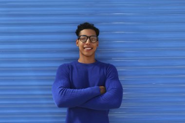 İspanyol kökenli, gözlük takan ve kolları katlanmış mavi duvarın yanında duran ince formalı genç bir adam. Metin için boşluk kopyala, kapat, arkaplan.