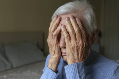 Başı ağrıyan yaşlı bir kadının portresini yakından çek, elleriyle yüzünü ört. Depresyon vücut dili. Metin ve arkaplan için boşluk kopyala.