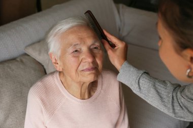 Yaşlı bir bayanın saçını tarayan tanınmamış bir kadın. Torun, büyükannenin saçını kesmesine yardım ediyor. Aile değerleri kavramı. boşluğu kopyala, arkaplanı kaybet.