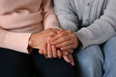 Yaşlı kadın ve kadın sosyal hizmet görevlisinin el ele tutuşması. Farklı yaşlardaki kadınlar birbirlerini teselli ediyorlar. Kapat, arkaplan, kopyala.