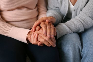 Yaşlı kadın ve kadın sosyal hizmet görevlisinin el ele tutuşması. Farklı yaşlardaki kadınlar birbirlerini teselli ediyorlar. Kapat, arkaplan, kopyala.
