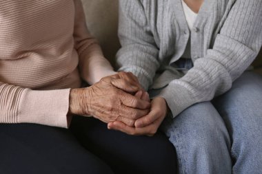 Yaşlı kadın ve kadın sosyal hizmet görevlisinin el ele tutuşması. Farklı yaşlardaki kadınlar birbirlerini teselli ediyorlar. Kapat, arkaplan, kopyala.