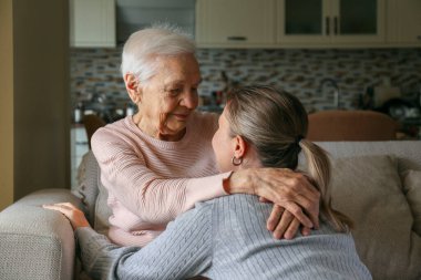 Büyükanne ve torun oturma odasında sarılıyorlar. Farklı yaşlarda iki yetişkin kadın. Aile değerleri kavramı. Kapat, kopyala boşluk, arkaplan.