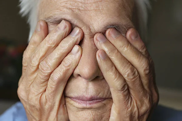 Close up portrait of elderly woman experiencing headache, covering her face with hands. Depression body language. Copy space for text, background.