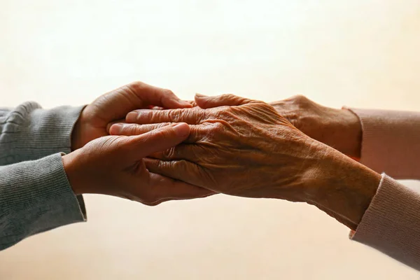stock image Cropped studio shot of elderly woman and female geriatric social worker holding hands. Women of different age comforting each other. Close up, background, copy space.