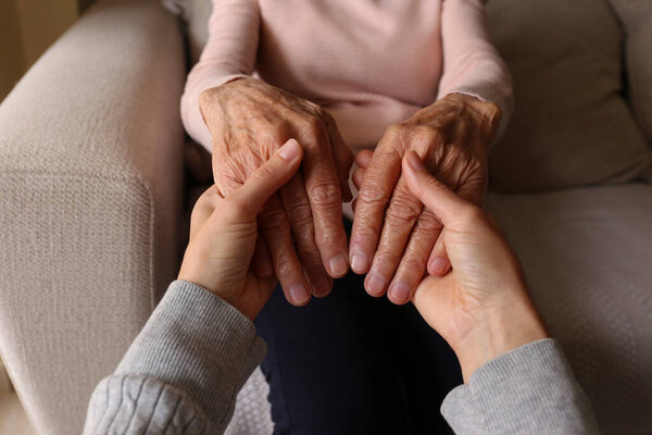 Cropped shot of elderly woman and female geriatric social worker holding hands. Women of different age comforting each other. Close up, background, copy space.