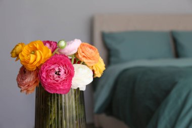 Komodinin üstündeki cam vazoda rengarenk bir ranunculus buketini yakın plan çek. Arka planda yeşil çarşaflar olan boş, yapılmamış bir yatak. Günaydın konsepti. Yatak odası doğal ışıkla dolu. Boşluğu kopyala