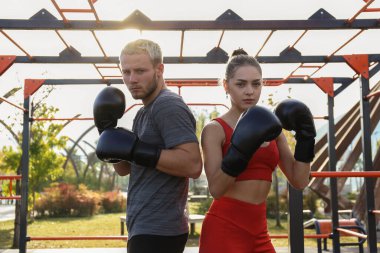 Açık hava spor salonunda kişisel grev koçuyla antrenman yapan genç bir kadın. Temiz havada boks seansı. Kadın kendini savunma dersinde teke tek oynuyor. Kapat, kopyala alanı, bar park arkaplanı.