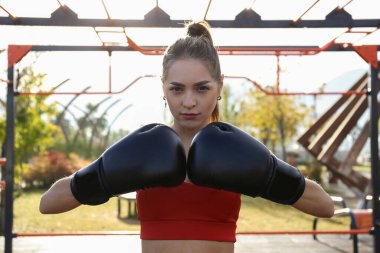Kadın boksör parkta hareketlerini çalışıyor. Dışarıda dövüş sanatları eğitimi alan genç bir kadın. Kapat, kopyala boşluk, arkaplan.