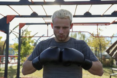 Boksör parkta hareketlerini çalışıyor. Spor salonunda dövüş sanatları eğitimi alan genç bir adam. Kapat, kopyala boşluk, arkaplan.