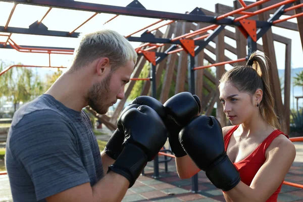 Young woman training with her personal striking coach at an outdoor gym. Boxing session at the fresh air. Female taking a one on one self defense class. Close up, copy space, bar park background.