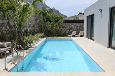 Güneşli bir günde, bir kır evinin arka bahçesindeki boş bir havuzun huzurlu görüntüsü. Kapat, boşluğu kopyala, arkaplanda dağlar.