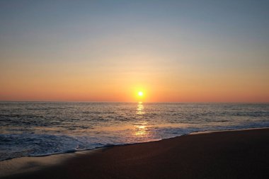 Güneşin sakin suyun üzerinde batışı, rüzgar desenleri ve berrak bulutsuz gökyüzü. Ufuk çizgisi olan okyanus görünümü, metin için bir sürü kopya alanı olan arkaplan.