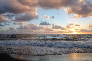 Güneşin güzel deniz manzarası gün batımında aydınlık dalgalar ve bulutlu gökyüzü ile denizin üzerinde batıyor. Ufuk çizgisi olan okyanus görünümü, metin için bir sürü kopya alanı olan arkaplan.