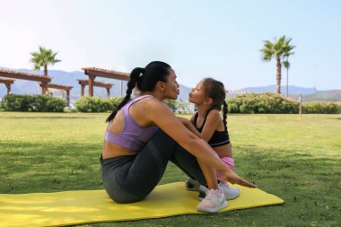 Anne ve kızı birlikte iyi vakit geçiriyorlar, fiziksel egzersizlerle kaynaşıyorlar. Küçük kız sabah egzersizi için annesine katıldı, parkta mekik çekti. Kapat, kopyala boşluk, arkaplan.