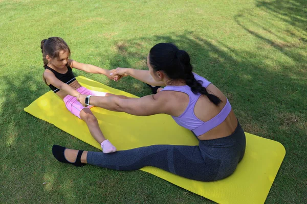 Mother and daughter spending quality time together, bonding through physical exercise. Little girl joined her mom for a morning yoga session, stretching in the park. Close up, copy space, background.