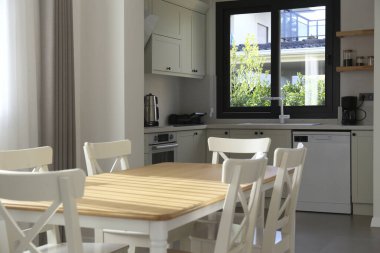 Boş yemek masası, beyaz dolap ve büyük pencereli şık bir açık plan. Boşluğu kopyala, arkaplan.