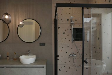 Modern banyo içi oval lavabo ve yuvarlak ayna, kolye armatürü ve cam duş kabini. Çağdaş minimalizm tarzı. Boşluğu kopyala, arkaplan.