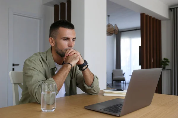 Bearded guy looking at the screen of his laptop. Adult education concept. Man taking an online course, watching a video lesson at home. Close up, copy space, interior background.