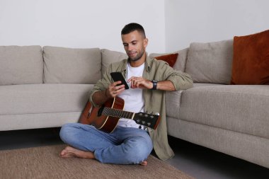 Sakallı müzisyen yerde oturuyor, Rousnought Salonunda akustik gitar çalıyor ve telefonuyla sosyal medya için içerik oluşturuyor. Arkaplan, kopyala boşluk, kapat
