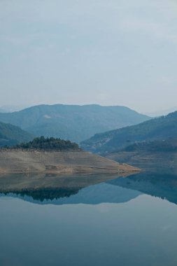 Gri bulutlu gökyüzü ile sakin sisli bir günde dağ gölünün güzel manzarası. Boşluğu kopyala, arkaplan.