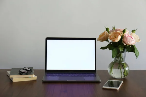 Home office concept. Feminine workspace with a blank screen laptop, phone, notebook and vase with roses. Close up, copy space, background.