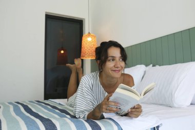 Genç ve güzel bir kadın elinde kitapla yatakta yatıyor. Düşünceli bir bayan evde kitap okuyor. Kapat, kopyala alanı, iç arkaplan.