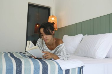 Genç ve güzel bir kadın elinde kitapla yatakta yatıyor. Düşünceli bir bayan evde kitap okuyor. Kapat, kopyala alanı, iç arkaplan.