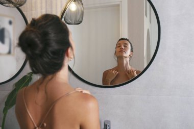 İpek gecelik giyen genç bir Orta Doğulu kadın aynaya bakıyor ve yüz masajı yapıyor. Sabah güzellik rutini konsepti. Kapat, kopyala boşluk, arkaplan.