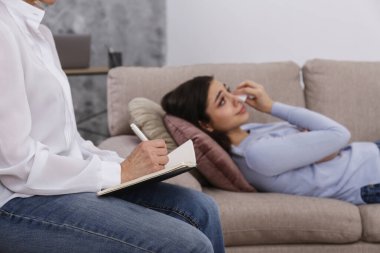 Yetişkin kadın terapist, depresyondaki genç bir kadınla seans sırasında notlar alıp göz yaşlarını siliyor. Kapat, kopyala boşluk, arkaplan.