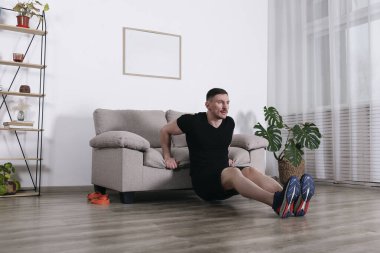 Vücut geliştirici vücut ağırlığı eğitimi, destek için kanepe kullanarak triseps dalışı. Genç adam oturma odasında jimnastik yapıyor. Kapat, kopyala boşluk, arkaplan.