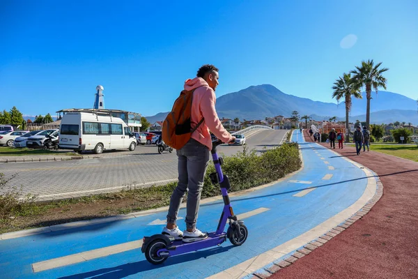 Güzel ada manzaralı mavi bir bisiklet yolunda e-scooter süren genç bir latin. Motorlu scooter 'la şehirden işe gidip geliyor. Boşluğu kopyala, tropikal hedef arkaplan.