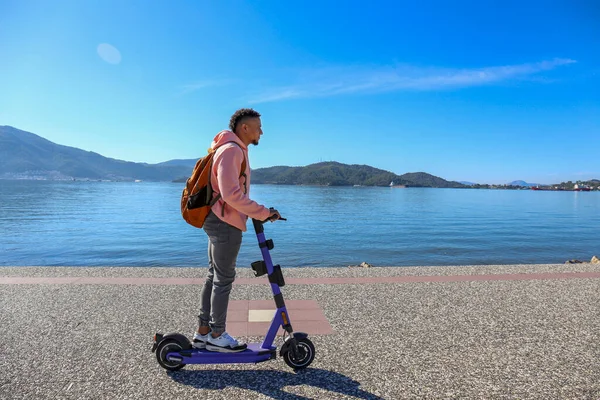Kıyı şeridi boyunca kiralık bir e-scooter 'la adaların güzel manzarası olan İspanyol genç bir adam. Boşluğu kopyala, deniz manzarası arkaplanı.