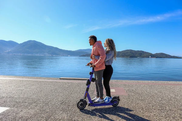 Adaların güzel manzarası ile gezinti alanında birlikte kiralık bir e-scooter süren genç Latin çift. Boşluğu kopyala,