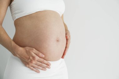 Hamile bir kadının destekleyici hamile sutyeni takıp çıplak karnına dokunurken çekilmiş bir fotoğrafı. Arkaplan, kopyala boşluk, kapat.