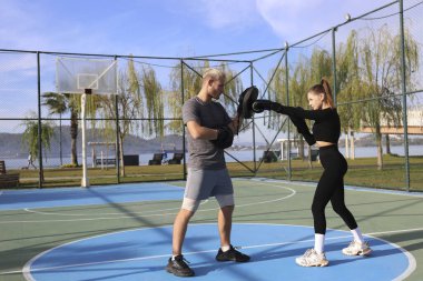 Kişisel antrenörüyle antrenman yapan ve açık hava spor salonunda yumruk tokuşturan genç bir kadın. Temiz havada boks seansı. Kapat, kopyala boşluk, arkaplan.