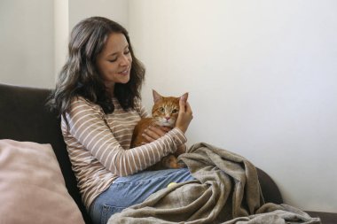 Esmer, genç bir kadın kurtarıcı kızıl kedisiyle evde oynuyor. Boşluk arkaplanı kopyala.