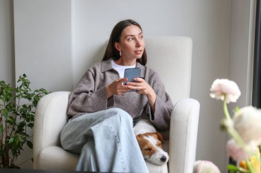 Evde köpeğiyle telefonu kaydıran genç bir kadın. Boşluğu kopyala, arkaplan.