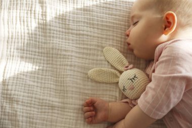 Pembe pijamalı sevimli bebek oyuncağıyla huzur içinde uyuyor. Boşluğu kopyala, arkaplan.