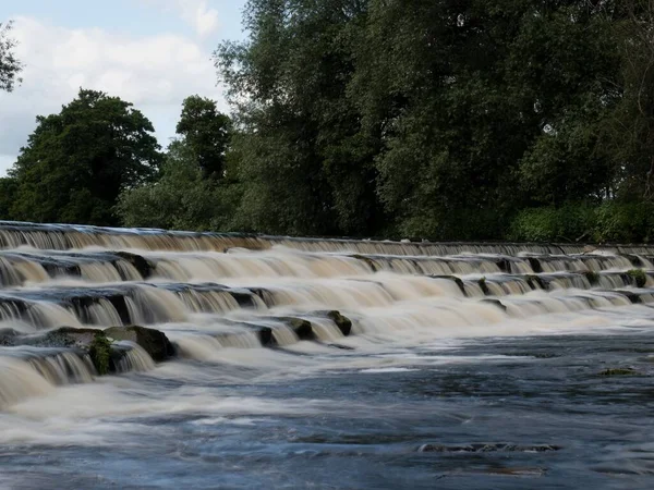 stock image A beautiful weir across the river Wharfe at Burley-in-wharfedale in England. The weir is in 4 steps and the flow is slow as the river isn't running fast. It is a lovely, sunny Summers day.