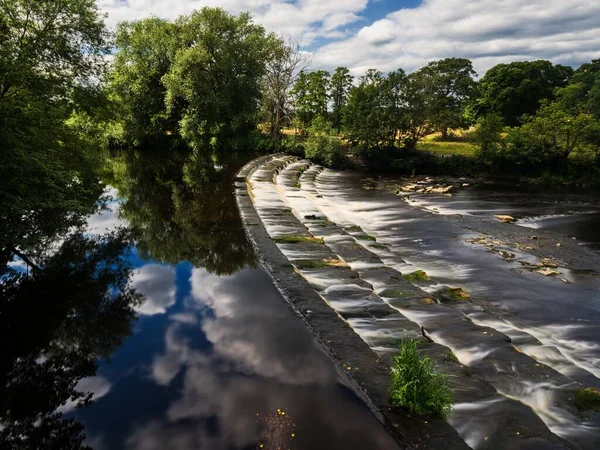 Wharfe Nehri 'nin karşısındaki Burley-in-Wharfedale, İngiltere' de güzel bir giysi. Weir 4 adımda ve nehir hızlı akmadığı için akış yavaşlıyor. Güzel, güneşli bir yaz günü..