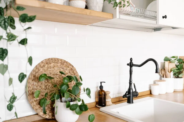 View on white simple modern kitchen in scandinavian style, kitchen details, houseplants in interior, wooden table, white ceramic brick wall background